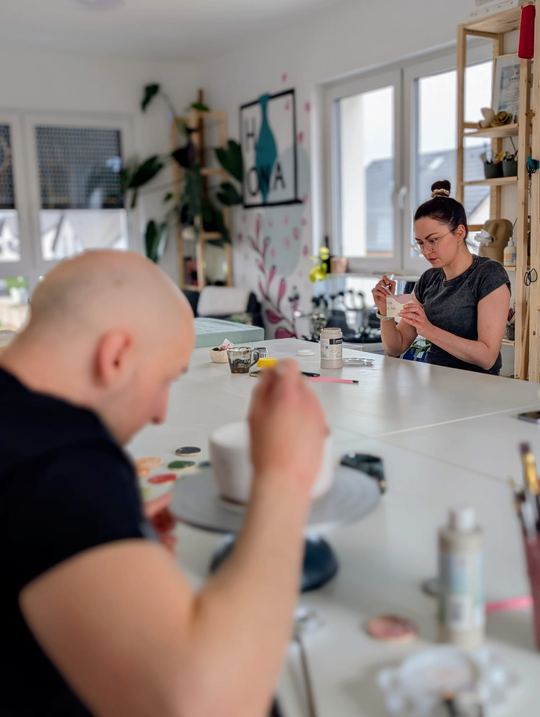 Uczestnik i uczestniczka malujący ceramikę w pracowni